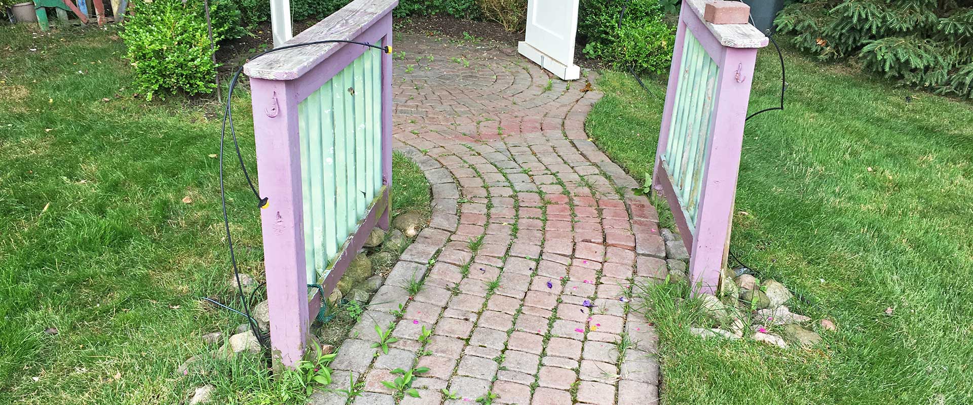 un-leveled brick paver walkway with weeds and moss growing through the joints